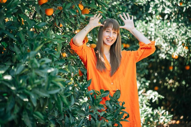 Happy girl in orange dress is showing funny getsure by holding hands around head in orange garden