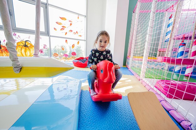 Happy girl playing at indoor play center playground sit and swings on an elephant rocking chair