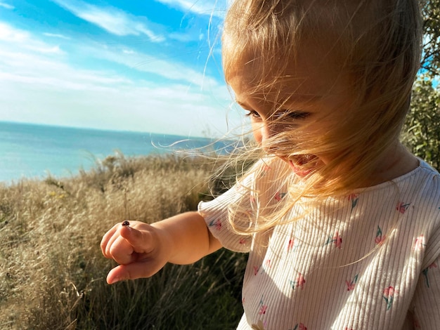 Happy girl plays with ladybug on finger and smiles