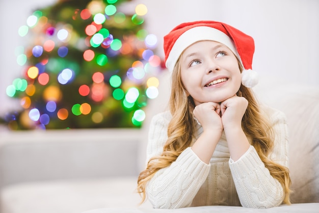 The happy girl in santa claus hat lay near the christmas tree