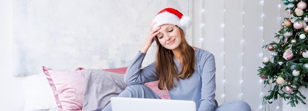 Happy girl in santa hat greets friends merry christmas video chat on laptop