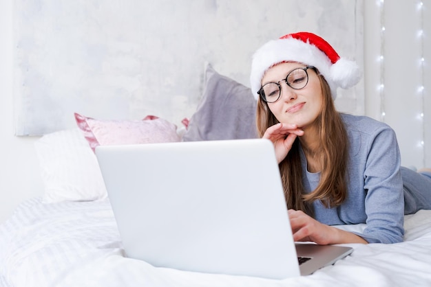 Happy girl in santa hat greets friends merry christmas video chat on laptop