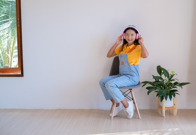 The happy girl sitting on a chair listening to music in minimal room at home