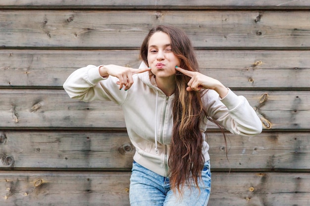 Happy girl smiling. Beauty portrait young laughing brunette woman posing with kiss face expression on wooden wall background. European woman. Positive human emotion