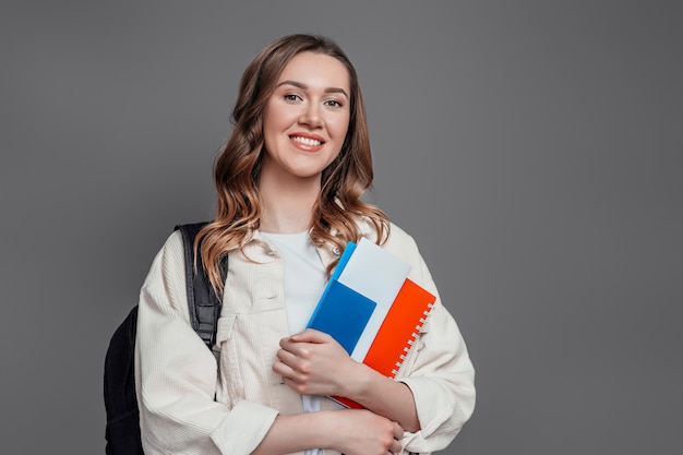 Happy girl student holding backpack book notebook passport isolated on a dark grey wall  immigration paperwork