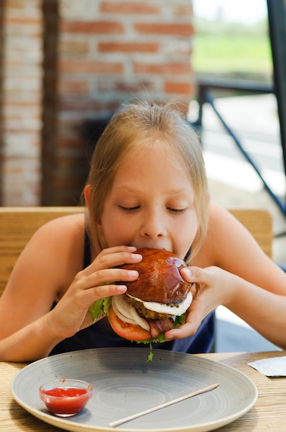 Happy girl, teenager eating a burger with a meat patty in a restaurant on a summer terrace. Food