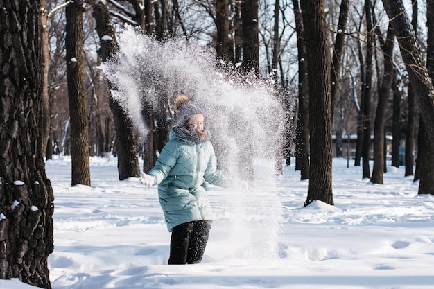 Happy girl in warm clothes throws snow in the winter forest Walk outdoors