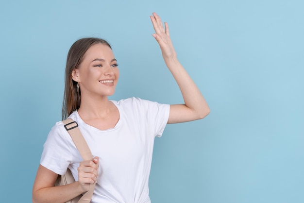 Happy girl waving greeting in white tshirt and striped pants with backpack