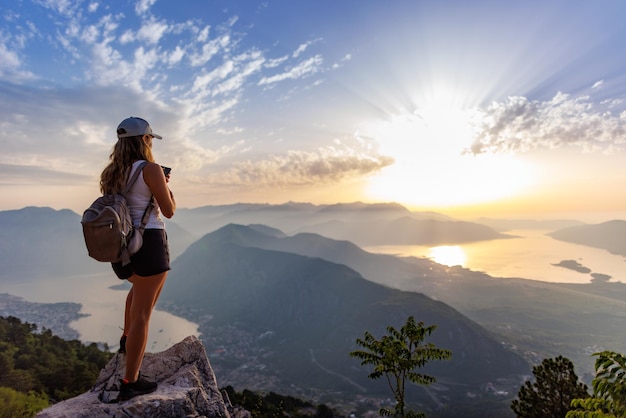 A happy girl with a backpack photographs the seascapes of montenegro from the top of the mountain