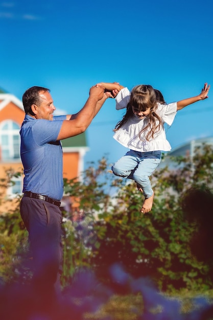 Happy girl with her father frolics on a summer day in nature A small child jumps high with the help of his father