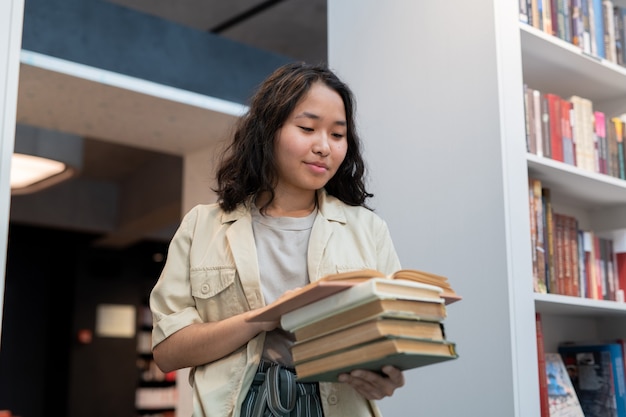 Happy girl with stack of books reading one of them