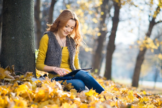 Happy girl with a tablet in the autumn park with yellow leaves