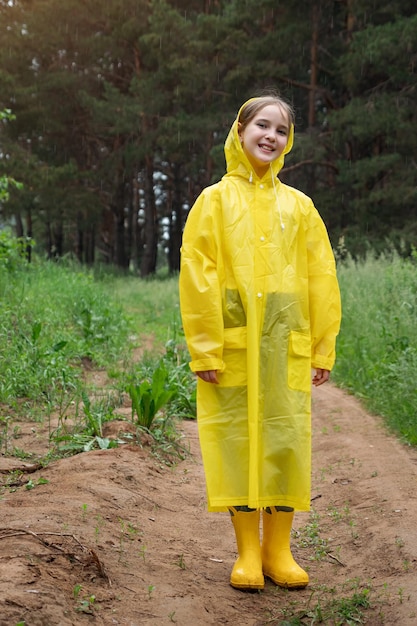 Happy girl in yellow raincoat walks enjoying summer nature