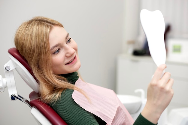 Happy girl young satisfied smiling woman patient with perfect smile looking at mirror after dentist