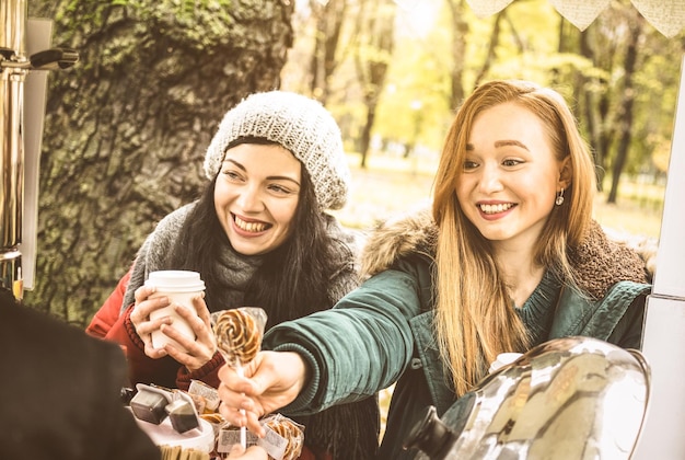 Happy girlfriends best friends sharing time together outdoors at coffee takeaway vendor in winter