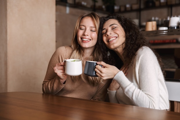 a happy girls friends sitting in cafe talking with each other drinking tea or coffee