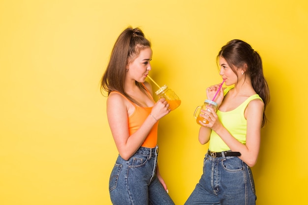 Happy girls smiling with drinks on yellow background