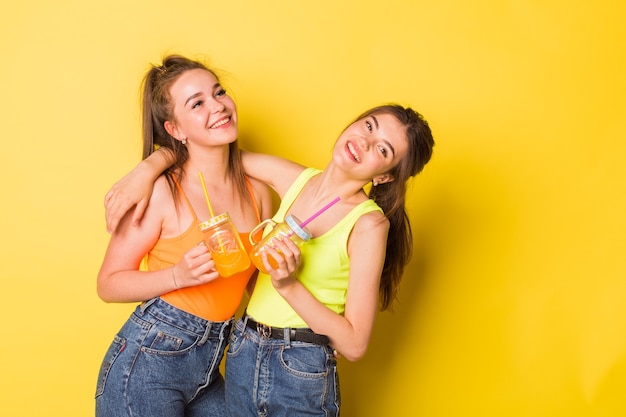 Happy girls smiling with drinks on yellow background