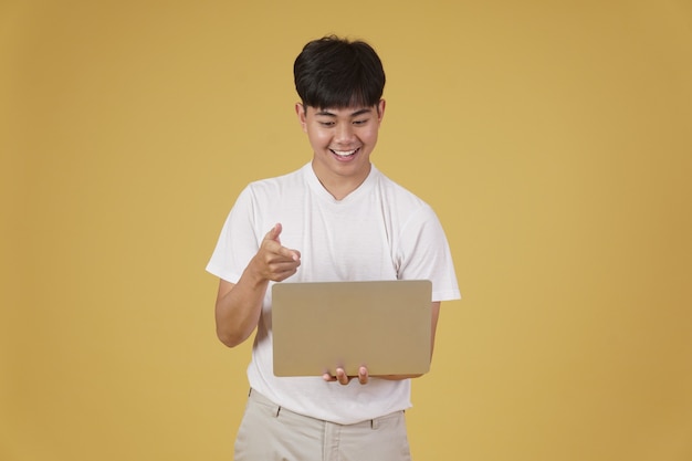 Happy glad rejoicing cheerful young asian man dressed casually holding pointing finger at laptop computer screen isolated