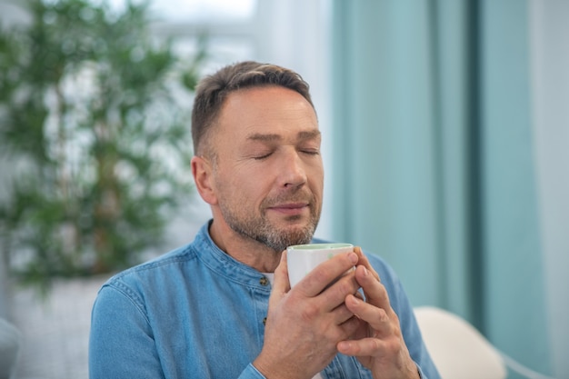 Happy good looking man with a cup in his hands, closing his eyes, in a good mood.