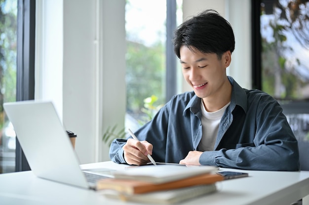 Happy and goodlooking young Asian male college student designing his artwork on digital tablet