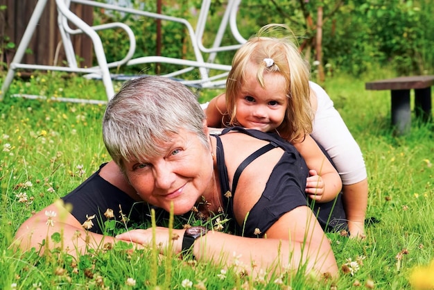 A happy grandmother and her granddaughter are lying on the green grass.