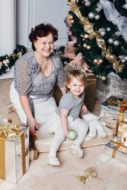 Happy grandmother with her granddaughter at home near the Christmas tree