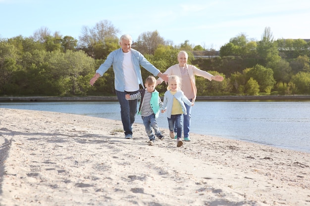 Happy grandparents playing with little children on river bank