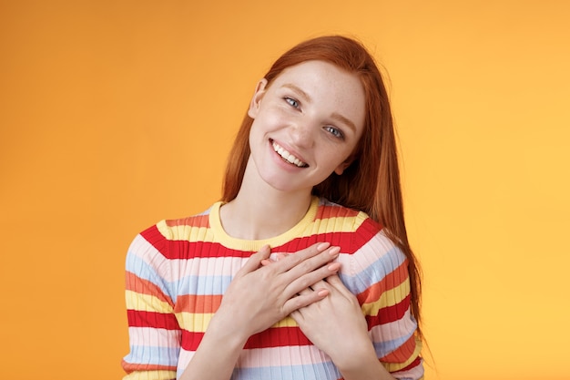 Photo happy grateful passionate stylish redhead european girl thanking dearest friend lovely sweet gift press palms heart smiling broadly tilting head amused gratefully appreciate, orange background.