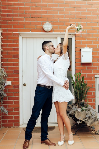 Happy groom and bride kissing hugging and raising her arm with her wedding bouquet after the ceremony. Wedding concept.