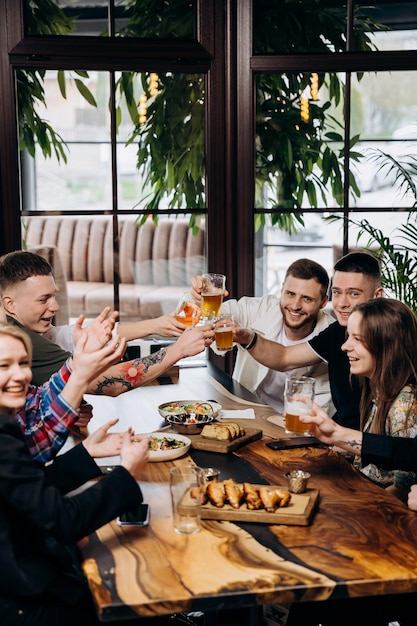 Happy group of friends drinking and clinking with beer and cocktails at brewery bar restaurant