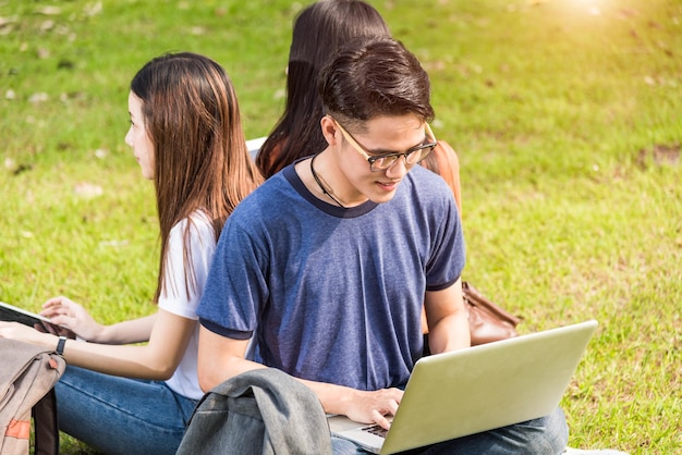 Happy group friends students sitting in park at college see laptop and tablet together