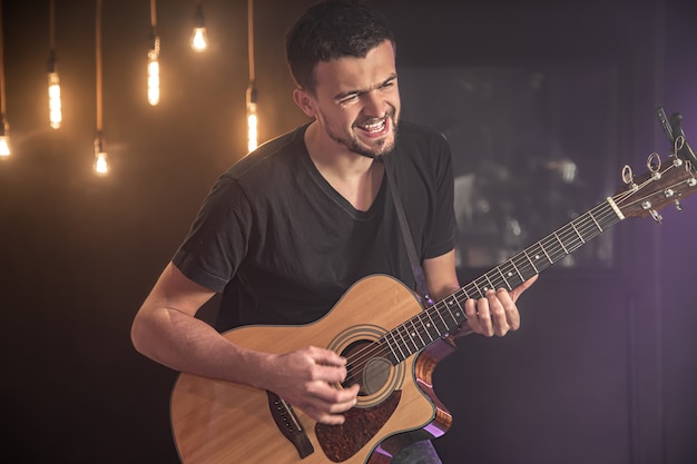 Happy guitarist in a black t-shirt plays an acoustic guitar at a concert against a blurred black background.