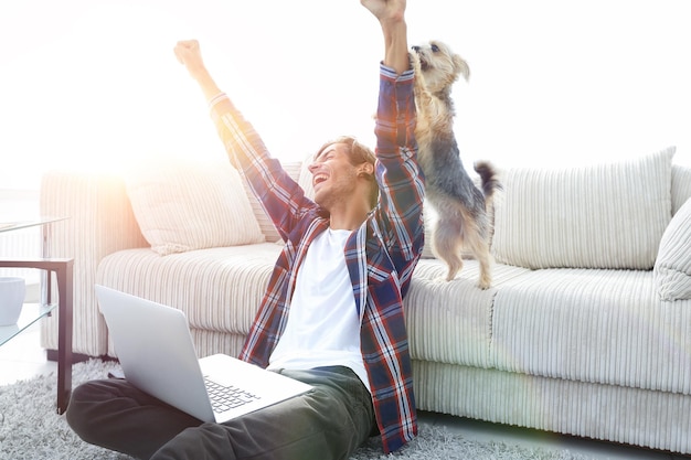 Happy guy exults with his dog sitting near the sofa in the living room