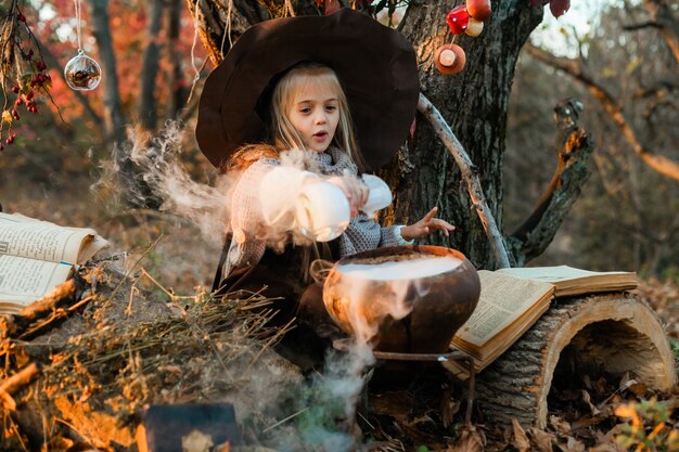 Happy Halloween. A cute girl in a witch costume is in the witch's den. Cute cheerful little witch brews a magic potion. Halloween.