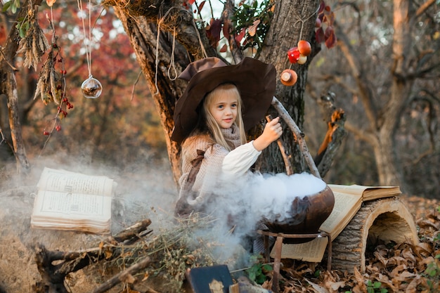 Happy Halloween. A cute girl in a witch costume is in the witch's den. Cute cheerful little witch brews a magic potion. Halloween.