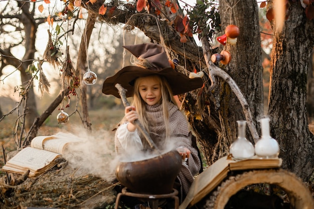 Photo happy halloween. a cute girl in a witch costume is in the witch's den. cute cheerful little witch brews a magic potion. halloween.