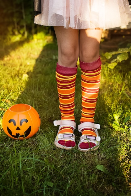 Happy Halloween day Little child is standing on grass in a witch costume near Jack pumpkin