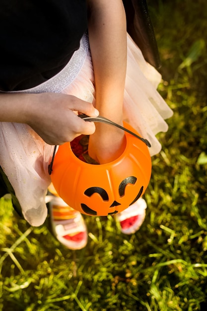 Happy Halloween day A little kid in a witch costume is looking for candy in his pumpkin Jack bucket