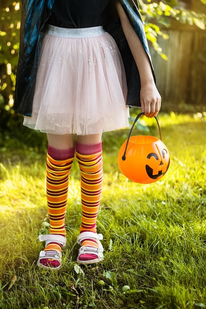 Happy Halloween day A little kid in a witch costume is looking for candy in his pumpkin Jack bucket