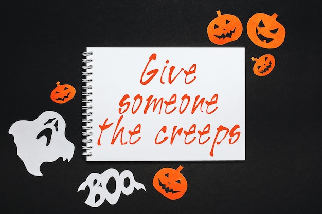 Photo happy halloween holiday concept. notepad with text give someone the creeps on black background with bats, pumpkins and ghosts