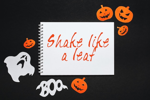 Photo happy halloween holiday concept. notepad with text shake like a leaf on black background with bats, pumpkins and ghosts