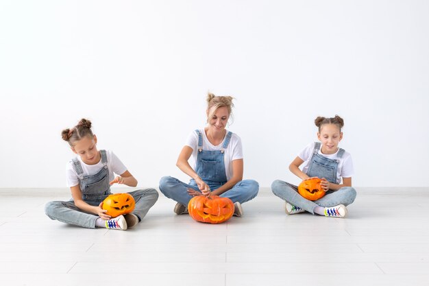 Happy halloween and holidays concept - A mother and her daughters with pumpkins. Happy family preparing for Halloween.