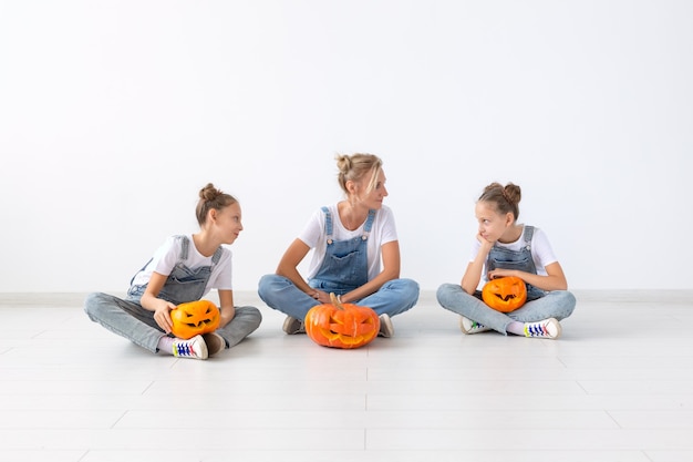 Happy halloween and holidays concept - A mother and her daughters with pumpkins. Happy family preparing for Halloween.