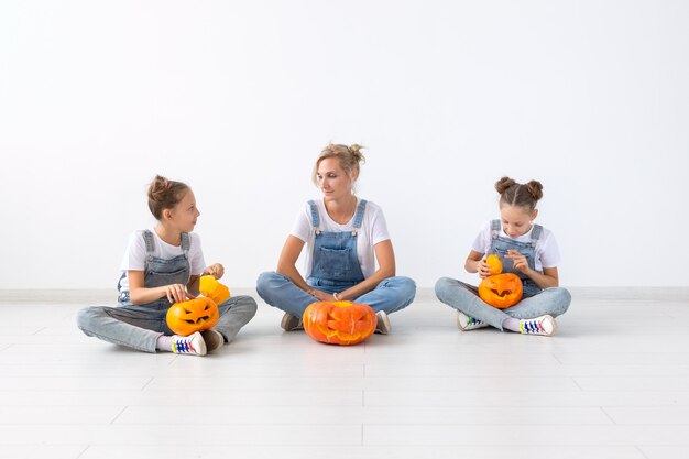 Happy halloween and holidays concept - A mother and her daughters with pumpkins. Happy family preparing for Halloween.