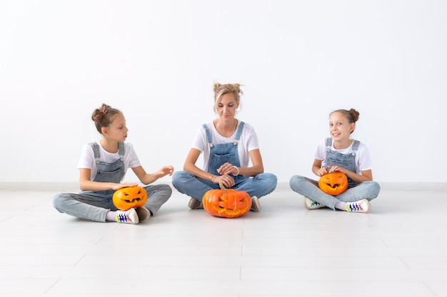 Happy halloween and holidays concept - A mother and her daughters with pumpkins. Happy family preparing for Halloween.