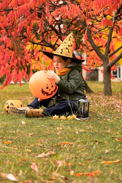 Happy Halloween kid playing with pumpkin balloon in park in autumn