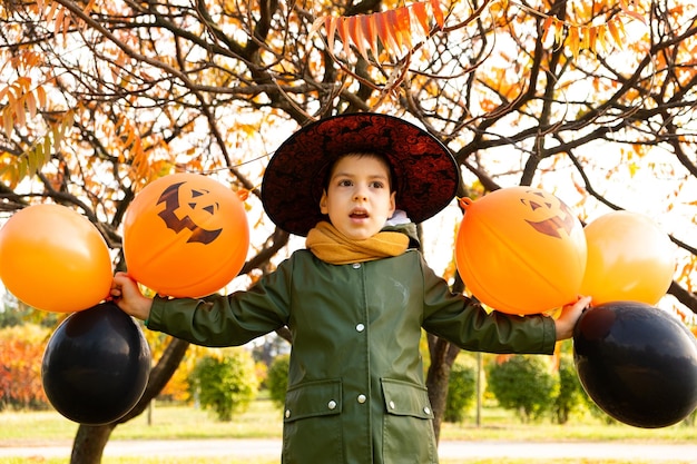 Happy Halloween kid playing with pumpkin balloons in park in autumn