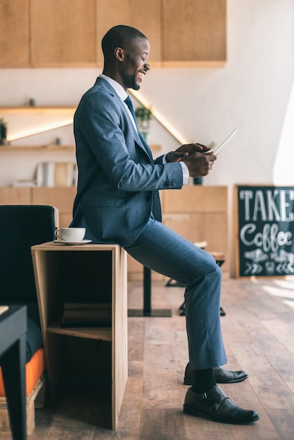 Happy handsome african american businessman using digital tablet during coffee break in cafe