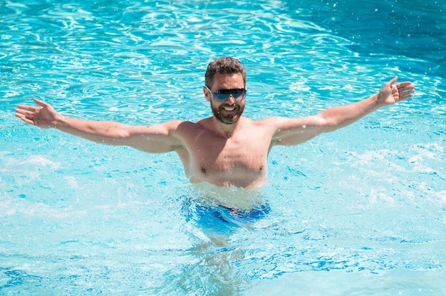 Happy handsome man in glasses swimming in pool on summer, vacation.